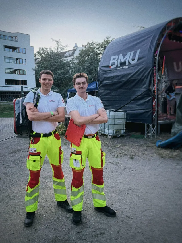 Zwei Sanitäter von SKALA Paramedics in Einsatzkleidung vor einer Festivalbühne