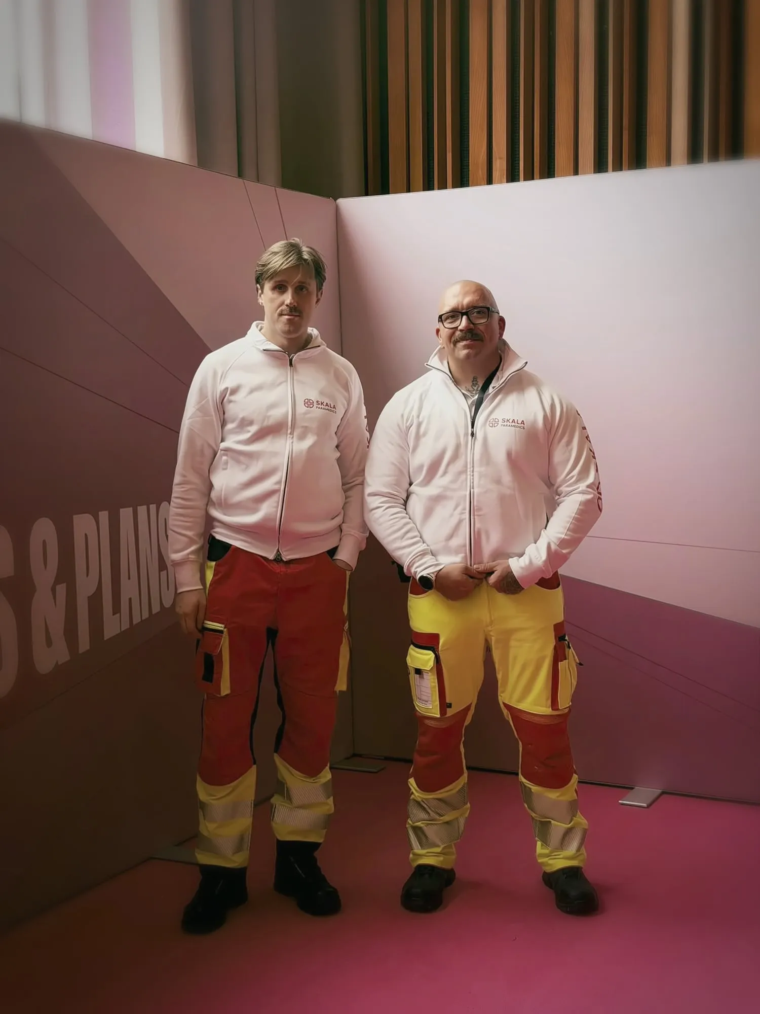 Zwei Einsatzkräfte von SKALA Paramedics vor einer rosa Fotowand im Kino International