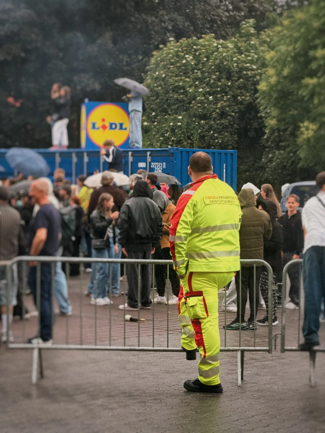 Sanitäter in Warnkleidung an der Absperrung eines Parkplatz-Raves vor großem Publikum