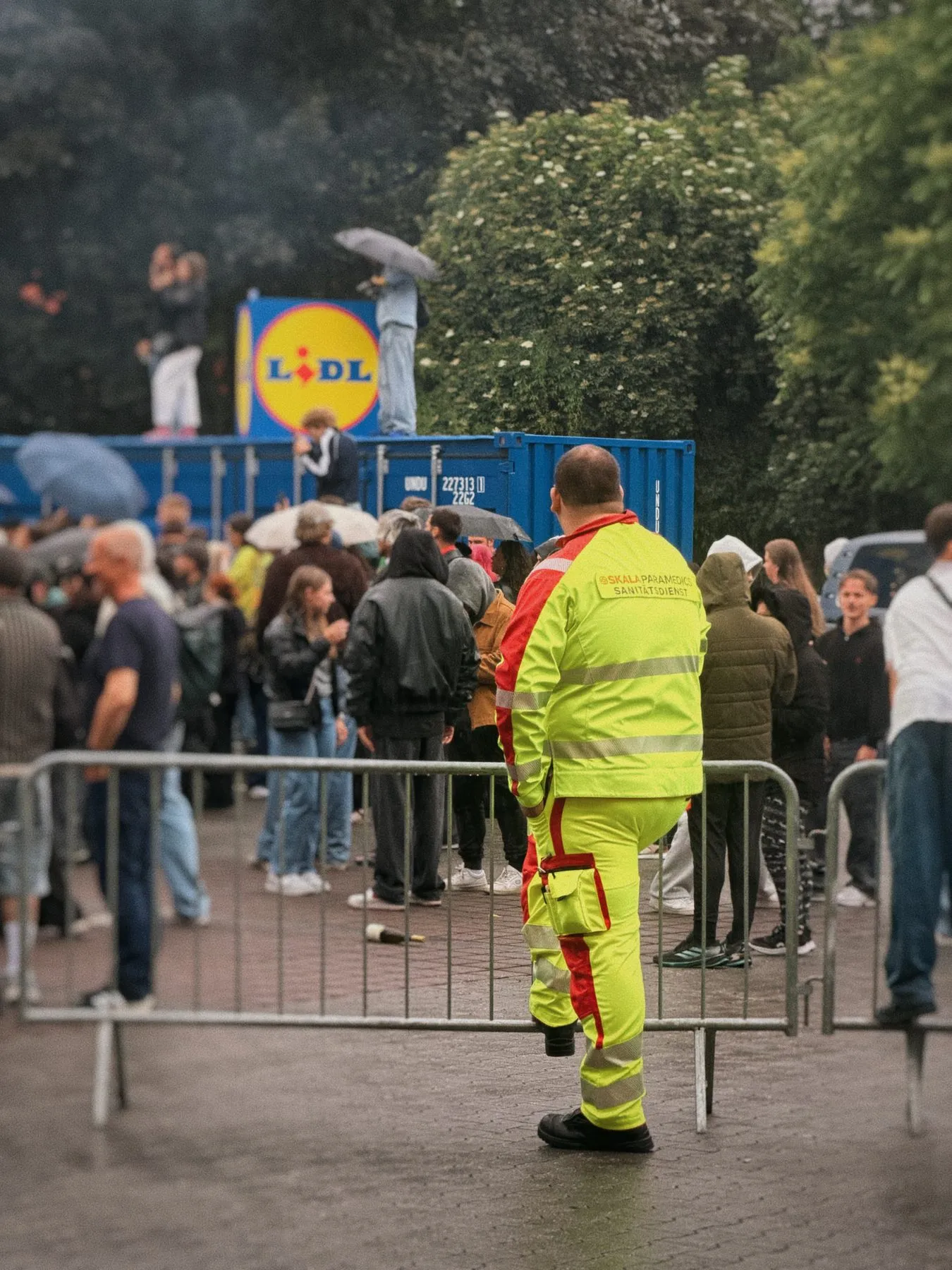 Sanitäter in Warnkleidung an der Absperrung eines Parkplatz-Raves vor großem Publikum