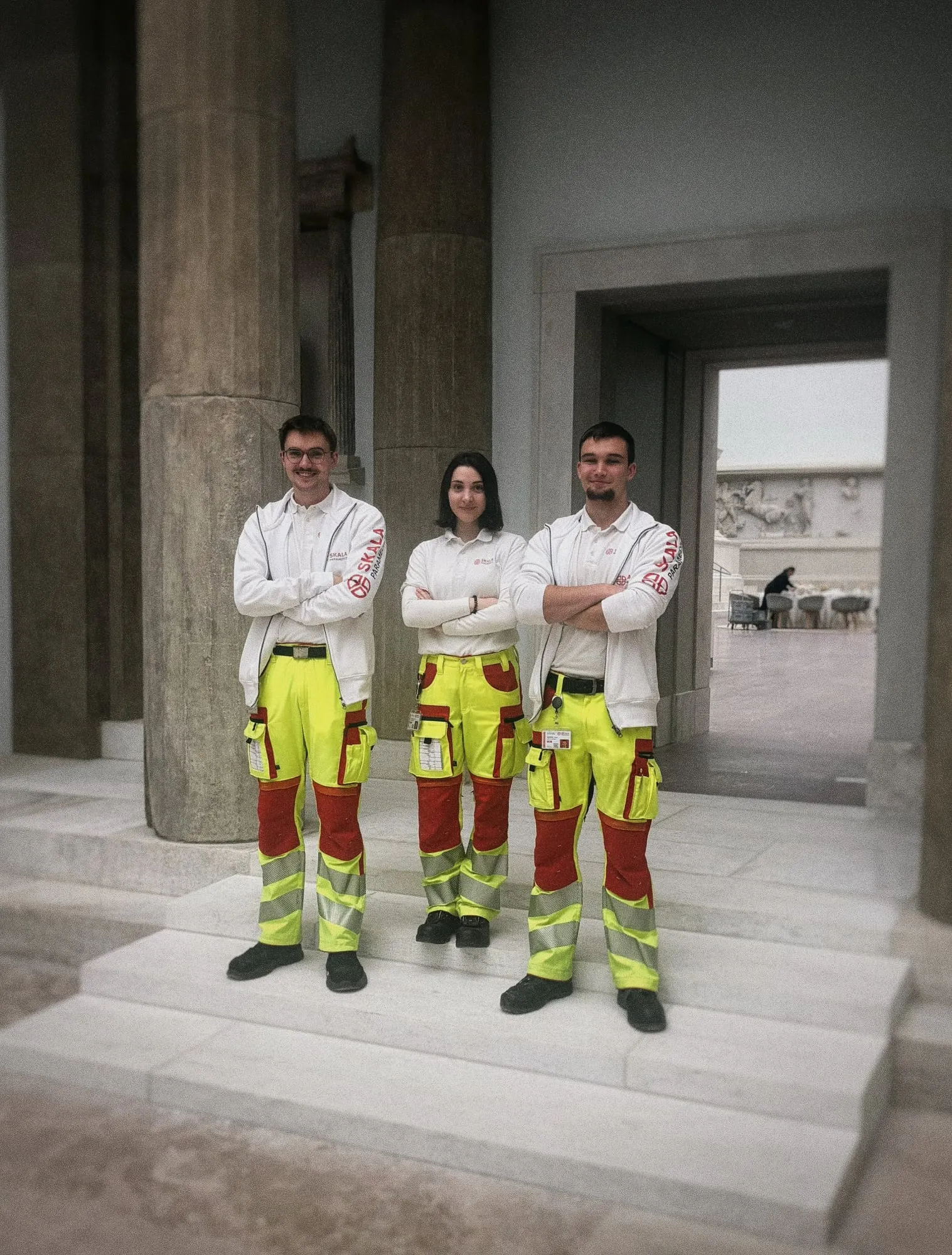 Drei Einsatzkräfte von SKALA Paramedics im Pergamonmuseum vor antiken Säulen, im Hintergrund der Pergamonaltar
