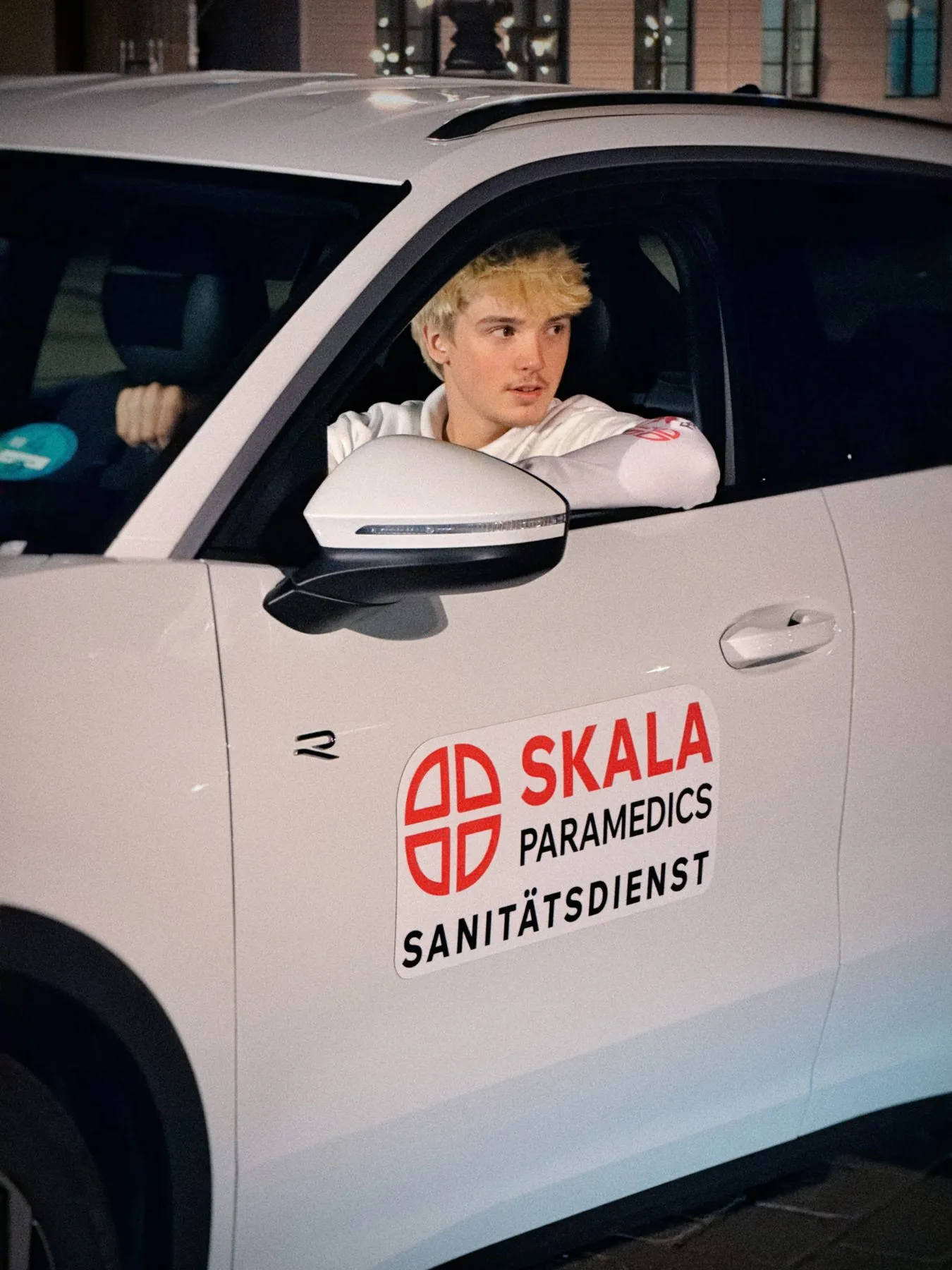 Sanitäter im Fahrerfenster des SKALA-Einsatzfahrzeugs mit Logo auf der Tür