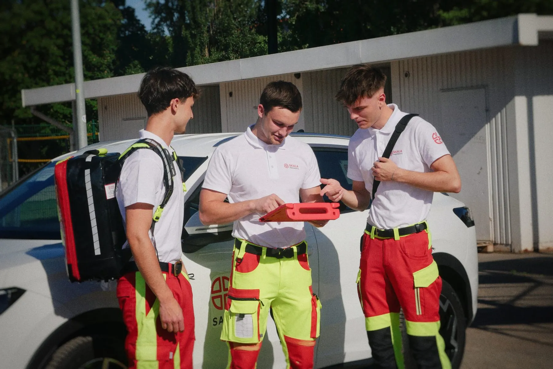 Drei Sanitäter besprechen einen Einsatz am Tablet neben dem Fahrzeug