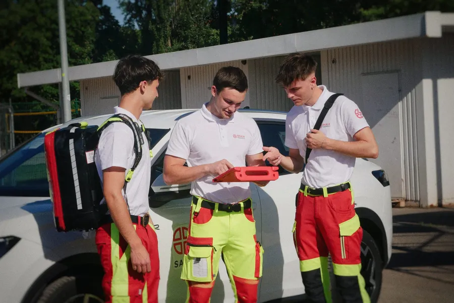 Drei Sanitäter besprechen einen Einsatz am Tablet neben dem Fahrzeug